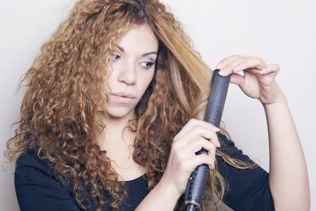 woman with curly hair holding hair straightener